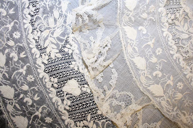 Nahaufnahme eines weißen Hochzeitskleids mit feiner, kunstvoller Spitzenverzierung in verschiedenen Formen und Mustern auf einem leichten, luftigen Stoff.