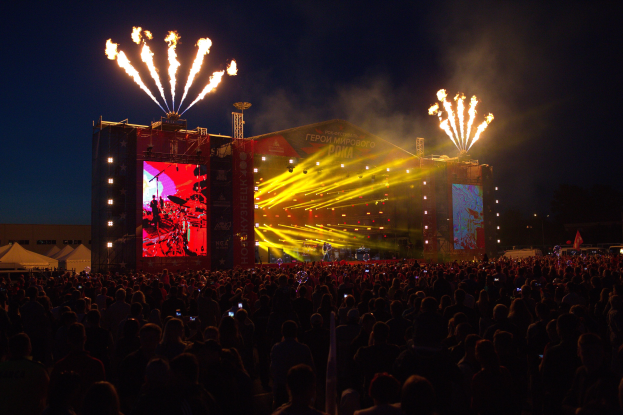 Große Menschenmenge bei einem nächtlichen Musikfestival mit beleuchteter Bühne und Feuerwerk am dunklen Himmel.