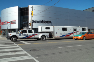 Ein Polizei-Lkw steht vor einem Gebäude mit Text darauf, mit einer Verkehrsampel mit einem Mast und Drähten im Vordergrund und Bäumen und einem klaren blauen Himmel im Hintergrund.