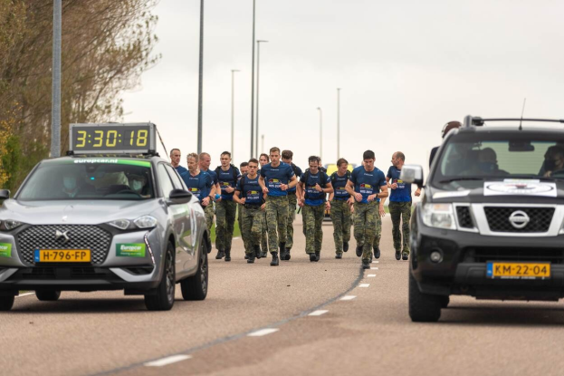 Eine Gruppe von Menschen, die auf einer Straße neben geparkten Autos laufen, mit Bäumen auf der linken Seite und Strommasten im Hintergrund, die an einer Europäischen Cross-Country-Challenge teilnehmen.