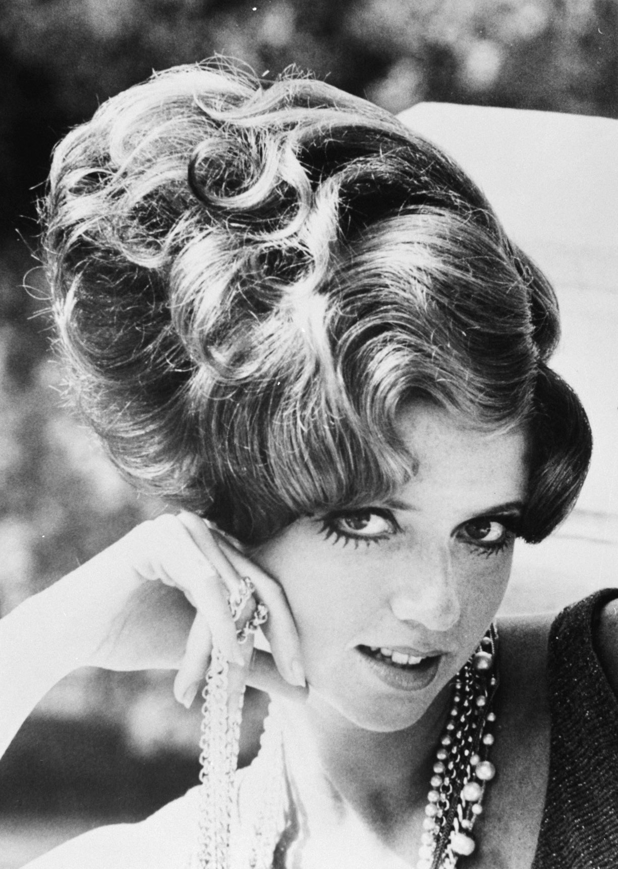 Schwarzes und weißes Foto von Prinzessin Diana in einem Kleid und Schmuck mit einem unscharfen Hintergrund.