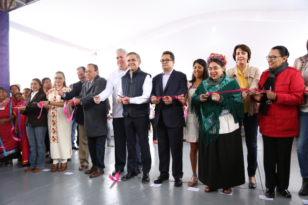 Eine Gruppe von Menschen, die mit Scheren vor einer Menschenmenge lächeln und eine Säule auf der linken Seite sowie verstreute Papiere auf dem Boden und ein weißes Tuch im Hintergrund haben.