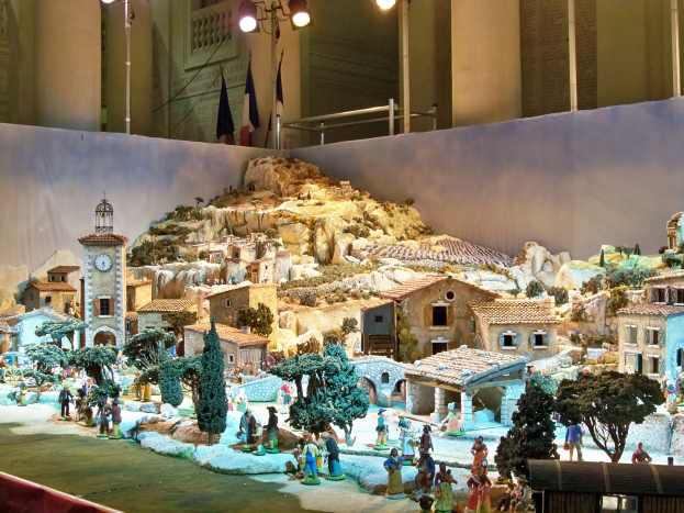 Ein detailliertes Modell einer Krippe, das in einem Museum ausgestellt ist und Figuren, Strukturen und beleuchtete Elemente enthält, die eine festliche Atmosphäre schaffen.